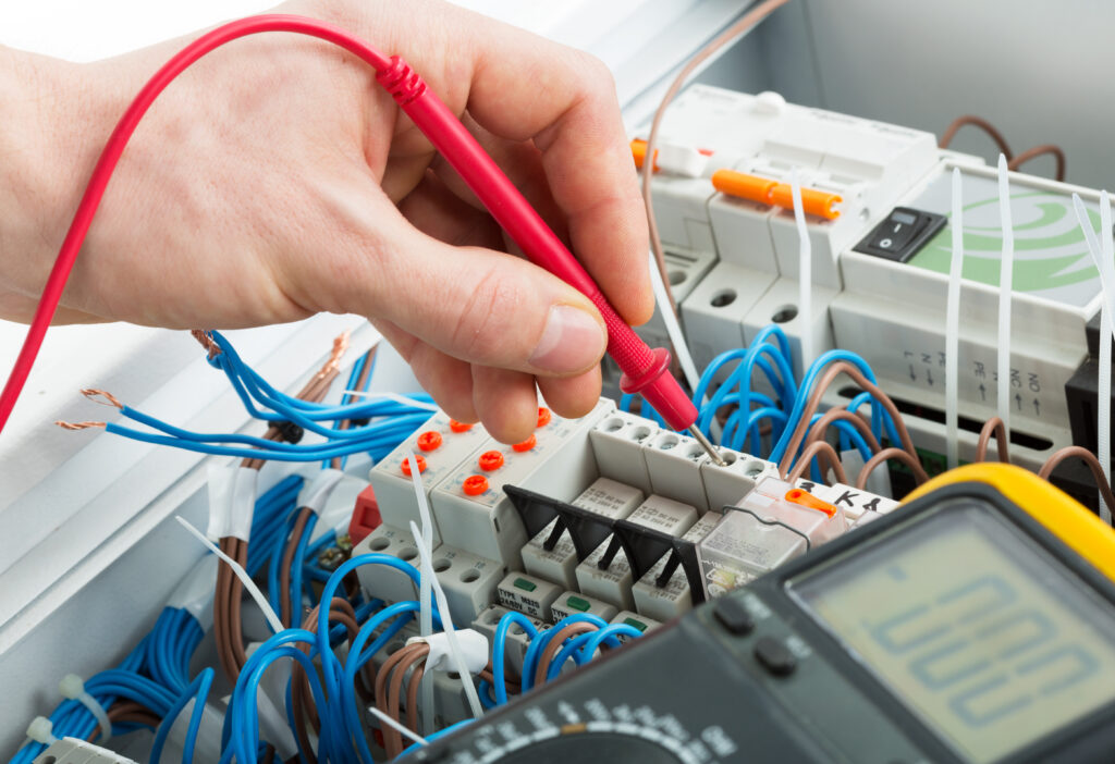 Hand of an electrician with multimeter probe at an electrical switchgear cabinet